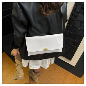 Sac bandoulière blanc en similicuir avec boucle dorée porté par un mannequin en veste