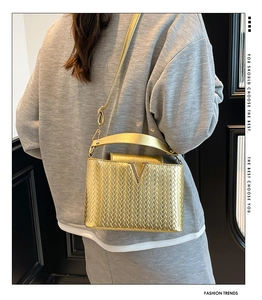 Detail of gold woven texture crossbody bag with metallic V-shaped logo on the flap