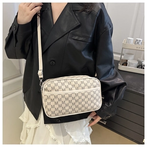 Close-up of cream crossbody bag with gray monogram print worn by a fashion model