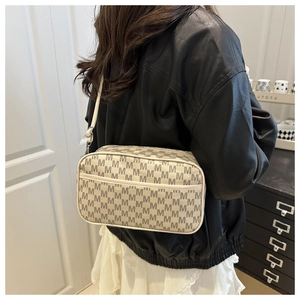 Detail showing cream crossbody bag with repeating M-pattern and front zipper pocket