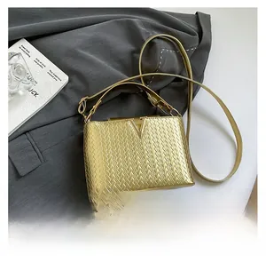 Détail d'un sac doré avec texture tissée en V et logo métallique sur fond de veste