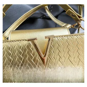 Détail macro du sac bandoulière en cuir tressé doré avec un logo V métallique proéminent