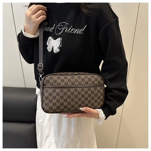 Dettaglio di borsa a tracolla marrone con stampa M indossata da modella in outfit casual