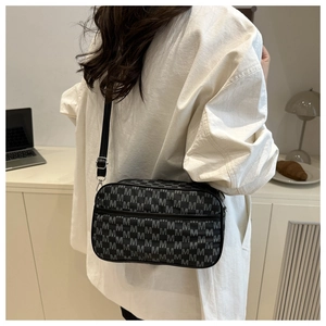 Detail of crossbody bag with M-letter pattern on adjustable shoulder strap and silver hardware
