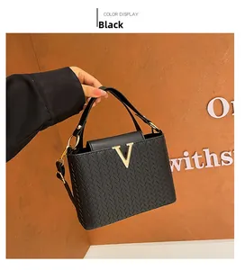 Close-up of black crossbody bag with woven texture and gold V-shaped metal logo buckle