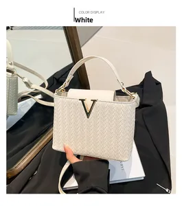 Close-up of white woven crossbody bag with gold V-shaped metal buckle detail