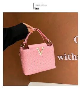 Close-up of pink woven handbag featuring a gold V-shaped buckle and elegant top handle
