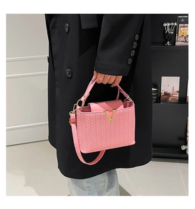 Sac à main rose à texture tissée avec boucle dorée en V dans un décor chic moderne