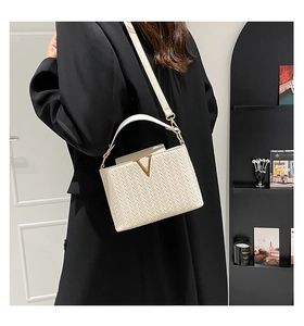 Détail du sac tressé crème avec boucle en V dorée porté sur un manteau en laine noir
