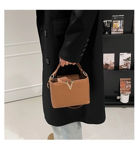 Détail d'un sac à main marron à texture tressée avec boucle en V dorée et poignée en cuir