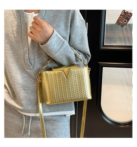 Gros plan d'un sac bandoulière tressé doré avec logo V métallique et texture élégante