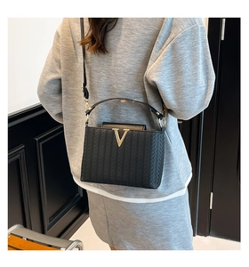 Detail of black woven texture bag with gold V-buckle and adjustable shoulder strap