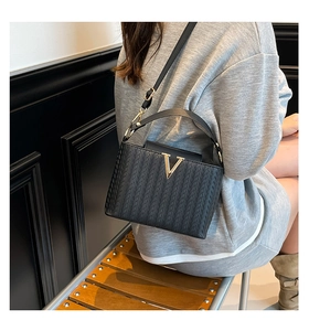 Détail du sac à main tissé noir avec une boucle métallique dorée en forme de V frappante