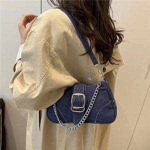 Borsa baguette in denim blu scuro con catena d'argento indossata su un trench beige