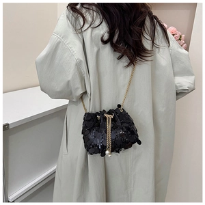 Crossbody view of black sequin bucket bag with gold chain strap on a stylish coat