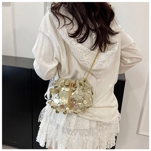 Détail d'un sac seau doré à paillettes avec bandoulière chaîne et pompon perle