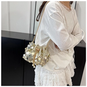 Detailed macro of gold sequin bucket bag featuring elegant white pearl drawstring charms