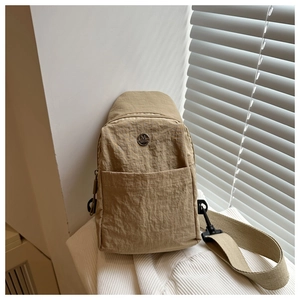 Détail du sac en nylon kaki avec logo métallique et bandoulière sur tricot blanc