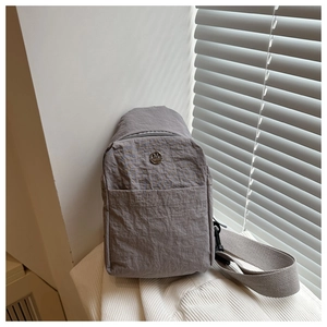 Gros plan d'un sac bandoulière en nylon gris avec texture et emblème M en métal