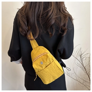 Detail of yellow nylon chest bag with pleated texture and round metal logo on model