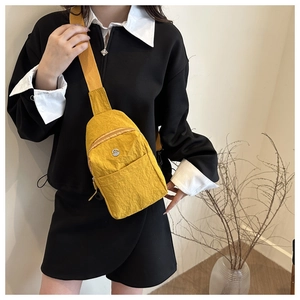 Detail of yellow nylon chest bag featuring round metal buckle and adjustable shoulder strap