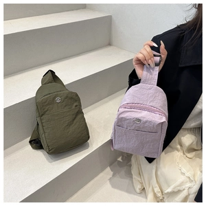 Gros plan de sacs bandoulière en nylon vert olive et lavande avec logo métallique sur escalier