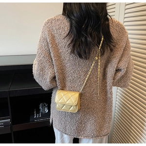 Gros plan d'un sac à chaîne doré matelassé porté dans une pièce au décor minimaliste