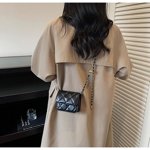 Détail d'un mini sac matelassé noir avec chaîne dorée porté sur un trench-coat beige