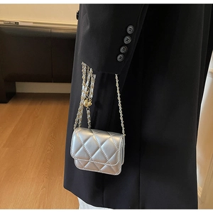 Gros plan du mini sac argenté matelassé avec chaîne dorée sur un blazer noir