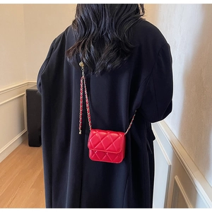 Détail d'un mini sac bandoulière matelassé rouge avec chaîne dorée sur manteau noir