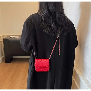 Détail d'un mini sac matelassé rouge avec chaîne porté sur un manteau noir élégant