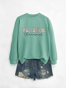 Flat lay of a mint green Radiation Therapist sweatshirt with distressed denim shorts
