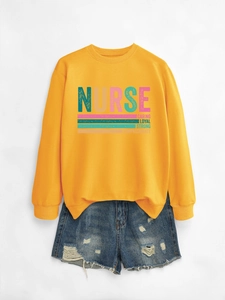 Flat lay of mustard yellow nurse sweatshirt featuring colorful text and distressed denim shorts