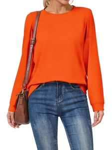 Detail of bright orange crewneck sweatshirt with ribbed cuffs and blue washed denim jeans