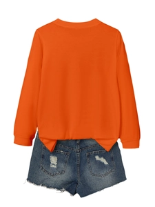 Rear view of long sleeve orange crewneck sweatshirt and distressed denim shorts with frayed hems