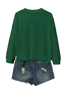 Detail of dark green long sleeve top featuring side slit and distressed denim shorts texture