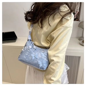 Détail du sac à bandoulière en dentelle bleu clair avec appliques papillons 3D et fleurs