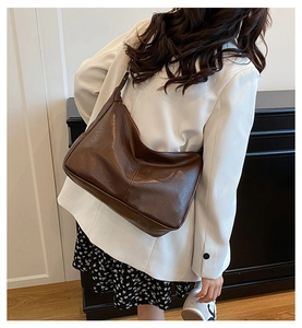 Sac hobo marron foncé en cuir plissé vintage porté par un mannequin en blazer blanc