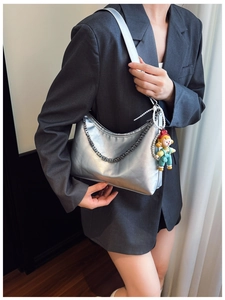 Detail of silver metallic hobo bag featuring chain strap and cute doll charm with pearls