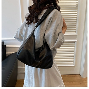 Vue latérale d'un sac hobo noir brillant avec large bandoulière sur un mannequin femme