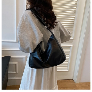 Model wearing large black leather hobo bag with knotted strap and lychee texture detail