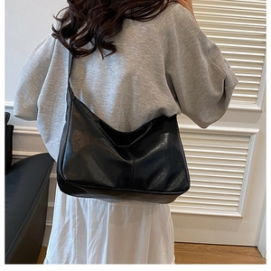 Detail of a large black glossy faux leather hobo bag worn by a model in a minimal room
