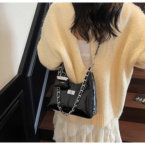 Detail of black patent leather shoulder bag with silver chain strap and mini pouch charm