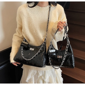 Close-up of black patent leather crossbody bag featuring silver chain and metal clasp