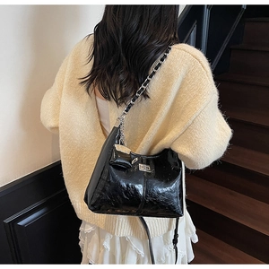 Detail of glossy black patent leather shoulder bag with silver chain and mini pouch charm