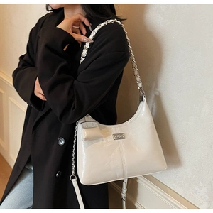 Detail of white patent leather shoulder bag featuring silver chain and mini coin purse charm