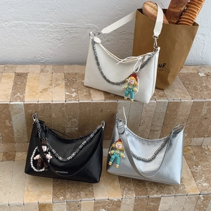Three crescent shoulder bags in white, black, and silver with metal chains and charms