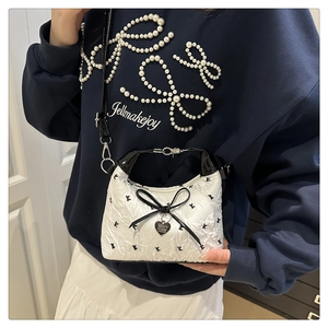 Detail of white pleated mini bag with black bow and heart pendant on navy sweatshirt