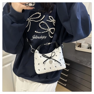 Detail of white quilted crossbody bag with black letter print and bow heart charm