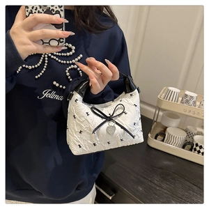 Detail of white pleated handbag with black bows and heart pendant in hand